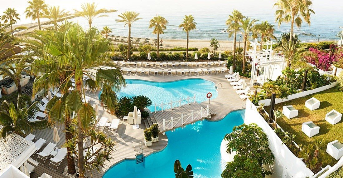 A beach club pool among palms on the Golden Mile, with the sea beyond