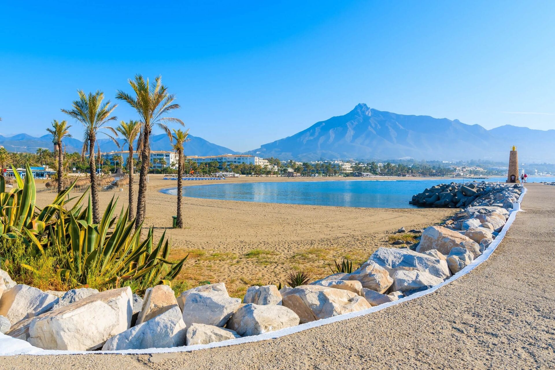 A sandy Marbella beach with palms, rocks and La Concha in the distance