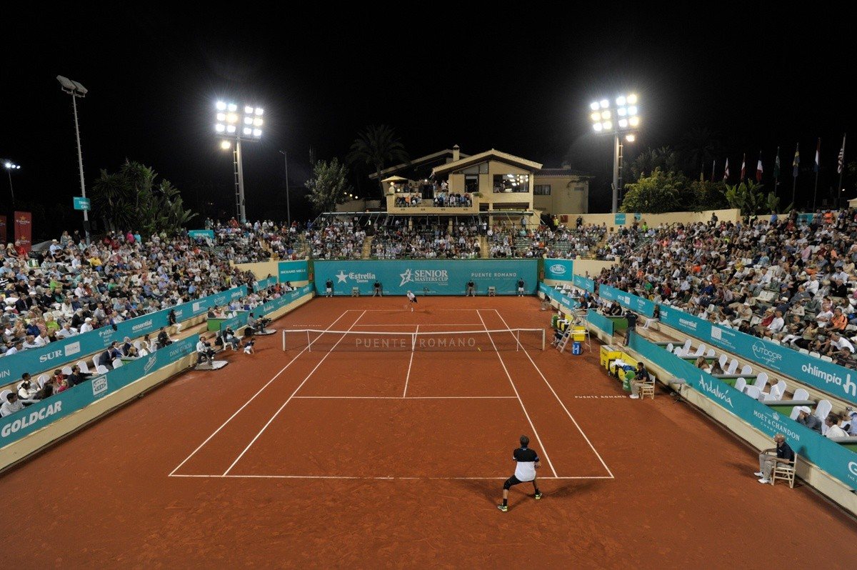 A floodlit clay tennis court with spectators in Marbella